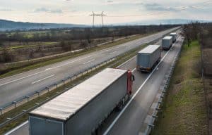 Convoy of Transportation trucks departing on a country highway under a sunset sky. Business Transportation And Trucking Industry.